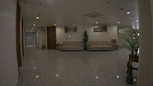A spacious lobby with a polished marble floor, two sofas, a potted plant, and artwork on the walls. - Royal Greens (Sikar)