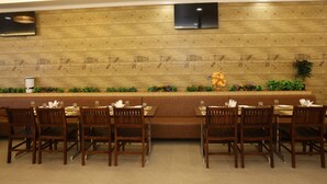 A restaurant with wooden panel walls, a flat-screen TV, and a long counter with chairs and tables. - Royal Greens (Sikar)