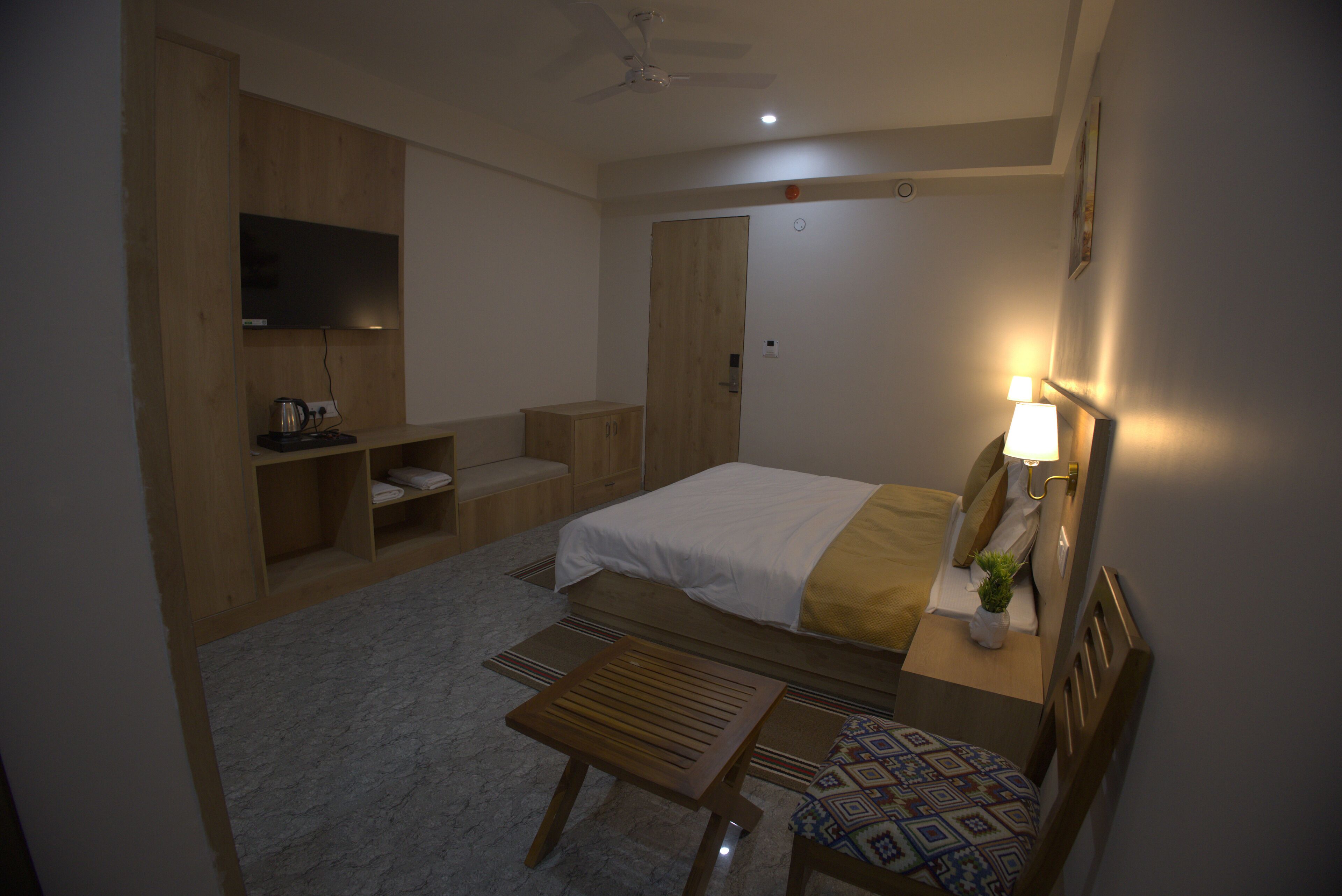 A hotel room with a bed, a desk, a chair, a television, and a ceiling fan.