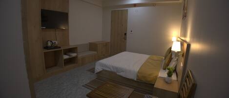 A hotel room with a bed, a desk, a chair, a television, and a ceiling fan.