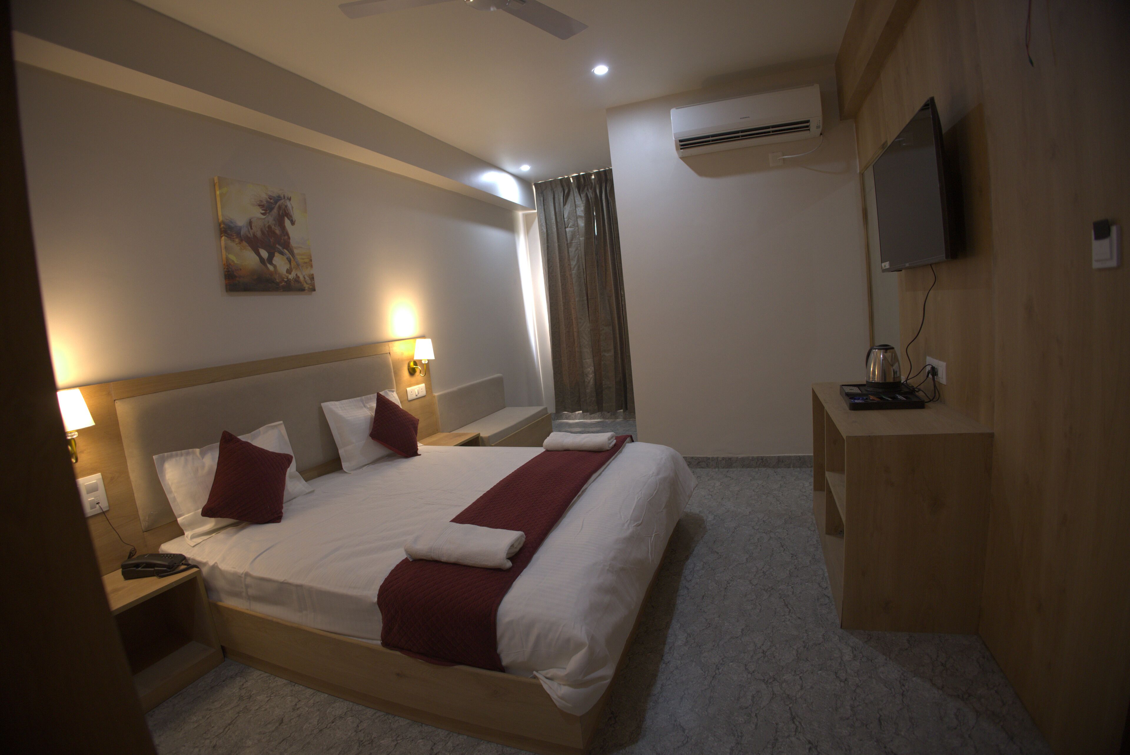A hotel room with a large bed, bedside lamps, a mounted TV, and an air conditioning unit.