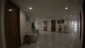 A hotel lobby with a marble floor, wooden doors, a reception desk, and wall-mounted artwork. - Royal Greens (Sikar)