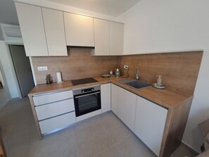A modern kitchen with white cabinets, a built-in oven, a sink, and a countertop. - Apartments Dolores (Rab)