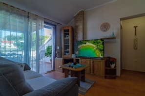 A living room with a sofa, a TV on a stand, a wooden cabinet, and a door with a 'WELCOME' sign. - Apartments Dolores (Rab)