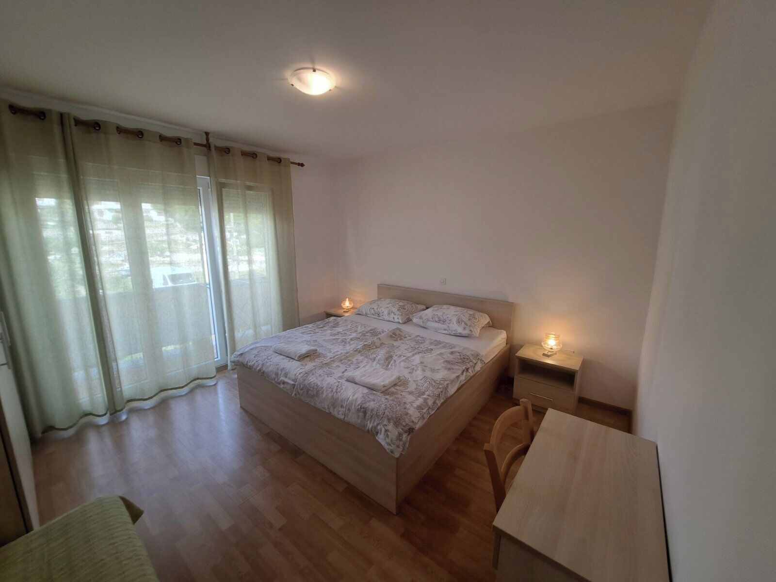 Ein Schlafzimmer mit einem hölzernen Bett, zwei Nachttischen mit Lampen, einem Holzstuhl und einem Schreibtisch.