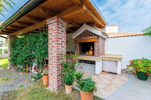 A brick outdoor kitchen with a chimney, surrounded by potted plants and a gravel area. - Apartments Dolores (Rab)