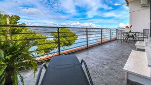 A balcony with a view of a bridge and trees, a table with chairs, and a potted plant. - Apartment Nela (Trogir)