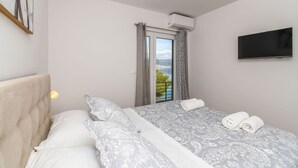 A bedroom with a bed, a TV, a window with curtains, and a painting on the wall. - Apartment Nela (Trogir)