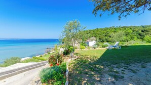 A coastal property with a paved pathway leading to a beach, surrounded by lush greenery and a clear blue sky. - Apartments Katica (Rab)