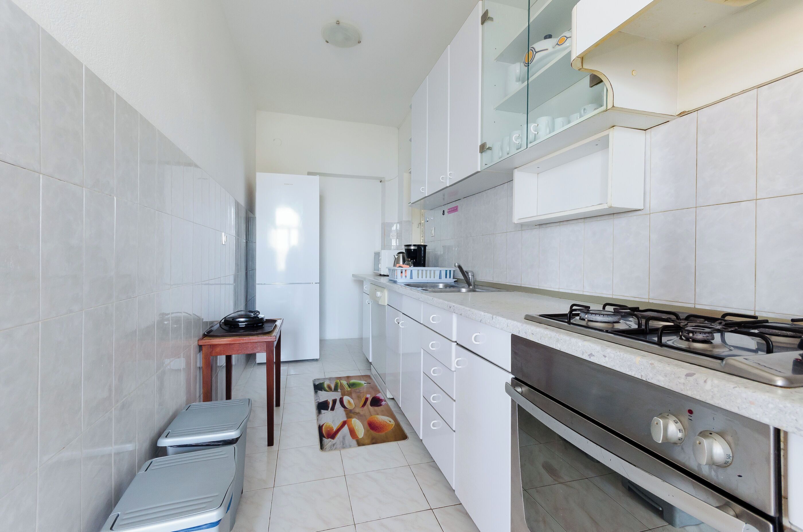 Una cocina compacta con armarios blancos, una estufa a gas y una pequeña mesa de madera.