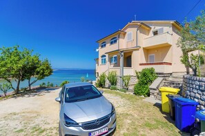 A two-story building with a beige facade, a car parked in front, and a clear view of the sea. - Apartments Katica (Rab)