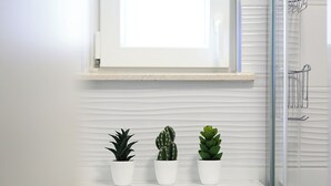 A bathroom with a white countertop, three potted plants, and a glass shower enclosure. - Apartment Romarin (Supetar)