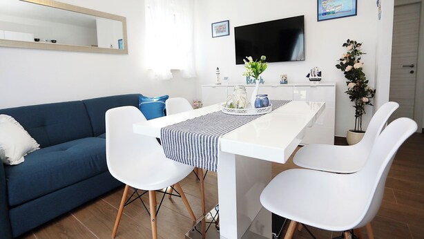 A modern living room with a sofa, dining table, chairs, a flat-screen TV, and decorative items. - Apartment Romarin (Supetar)