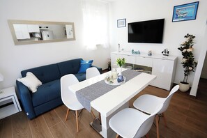 Un soggiorno moderno con un divano blu, un tavolo da pranzo bianco e sedie. Un televisore a schermo piatto è montato a parete sopra il tavolo.