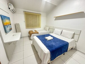 A hotel room with a bed, a bedside table, a window with blinds, a painting on the wall, and a thermostat. - Condomínio Portal do Atlântico (Porto Seguro)