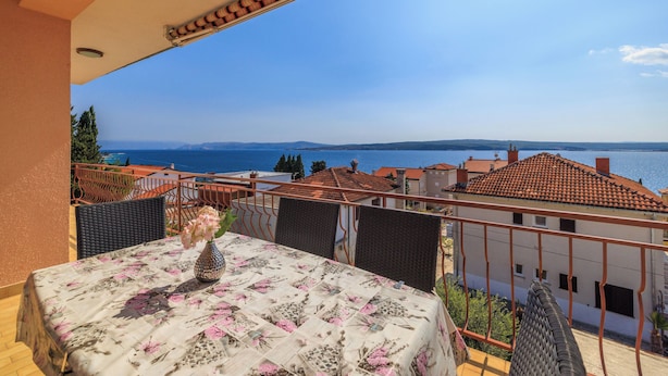Varanda com mesa posta para refeições, com vista para a costa, edifícios e o mar.