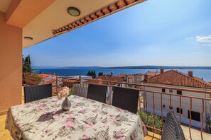 Un balcone con tavolo apparecchiato per mangiare, con vista sulla costa, edifici e mare.