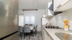 Uma cozinha moderna com área de jantar, apresentando piso xadrez, mesa com cadeiras, fogão e janela com cortinas leves.