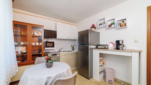 Cozinha compacta com geladeira, micro-ondas e cafeteira. Há uma mesa de jantar com cadeiras e um armário com portas de vidro.