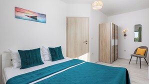 Una camera da letto moderna con un letto, biancheria da letto color petrolio, un quadro, un armadio e una sedia.