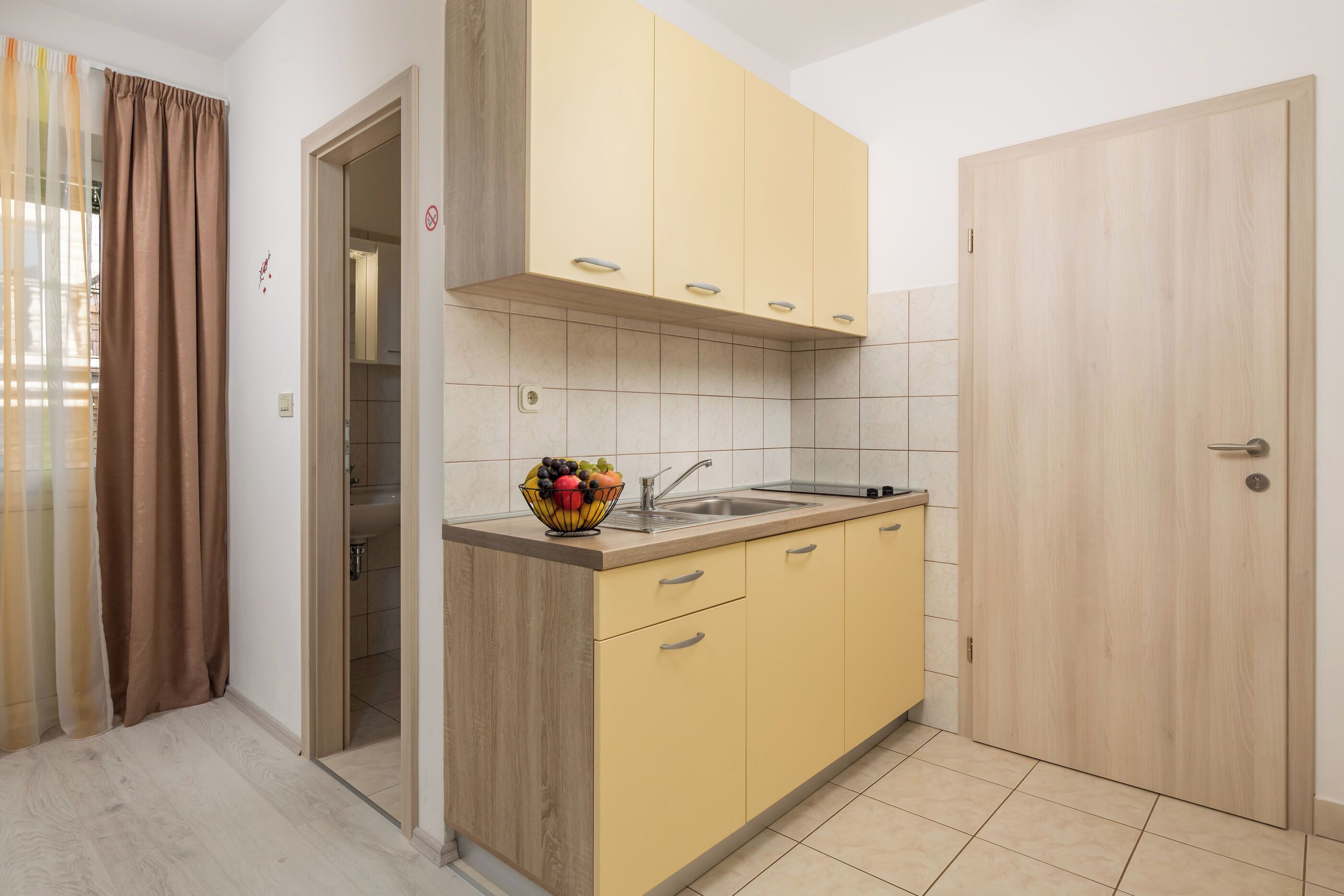 Una cocina compacta con armarios de madera, un lavamanos y un frutero sobre la encimera.