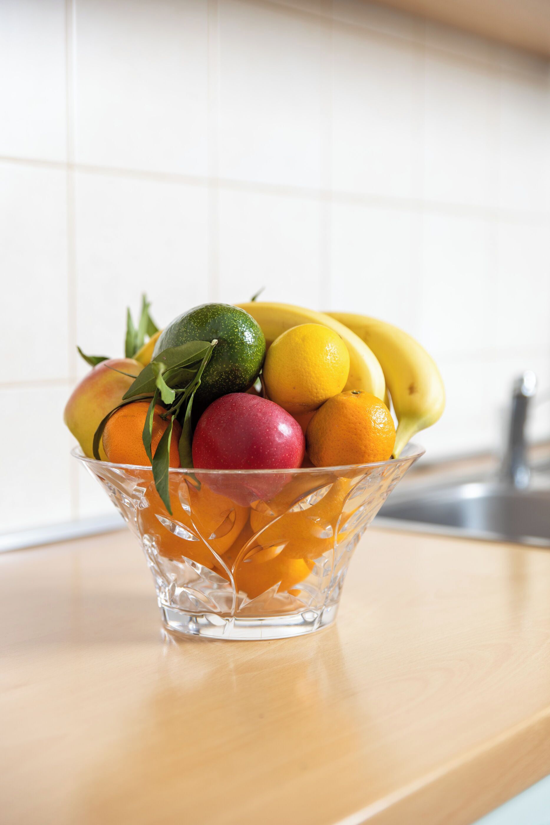 A clear glass bowl filled with various fruits on a kitchen counter.