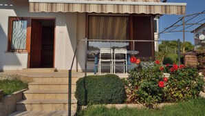A two-story house with a balcony, a wooden door, and a small garden with red flowers. - Apartments Boris (Umag)