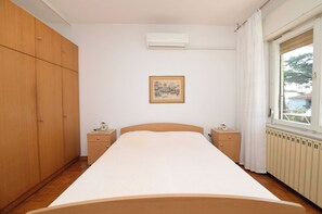 A bedroom with a large bed, wooden wardrobe, two bedside tables, a framed picture on the wall, and a window with curtains. - Apartment Boris (Umag)