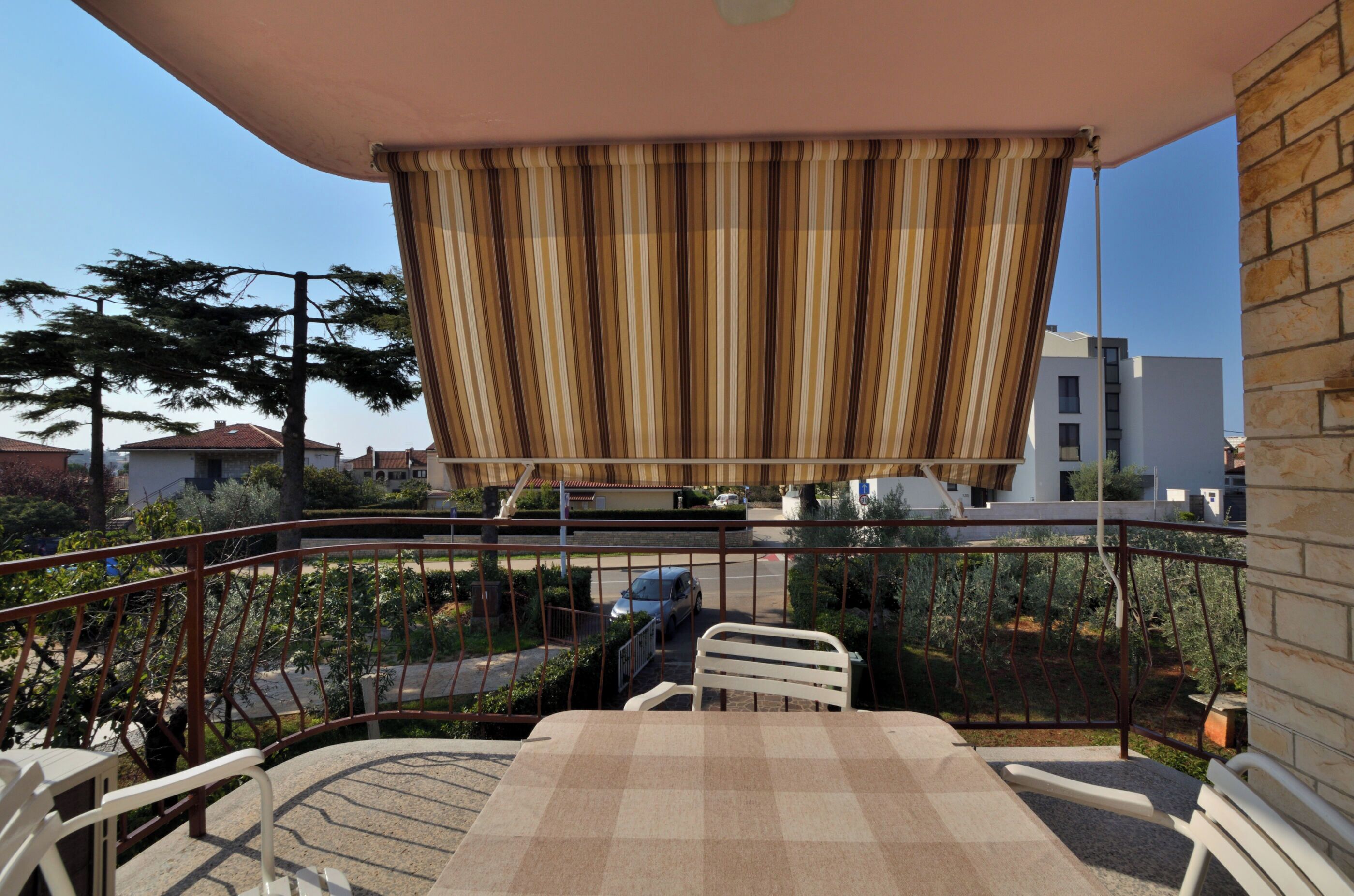 A balcony with a table and chairs, a striped curtain, and a view of a street with cars and buildings.