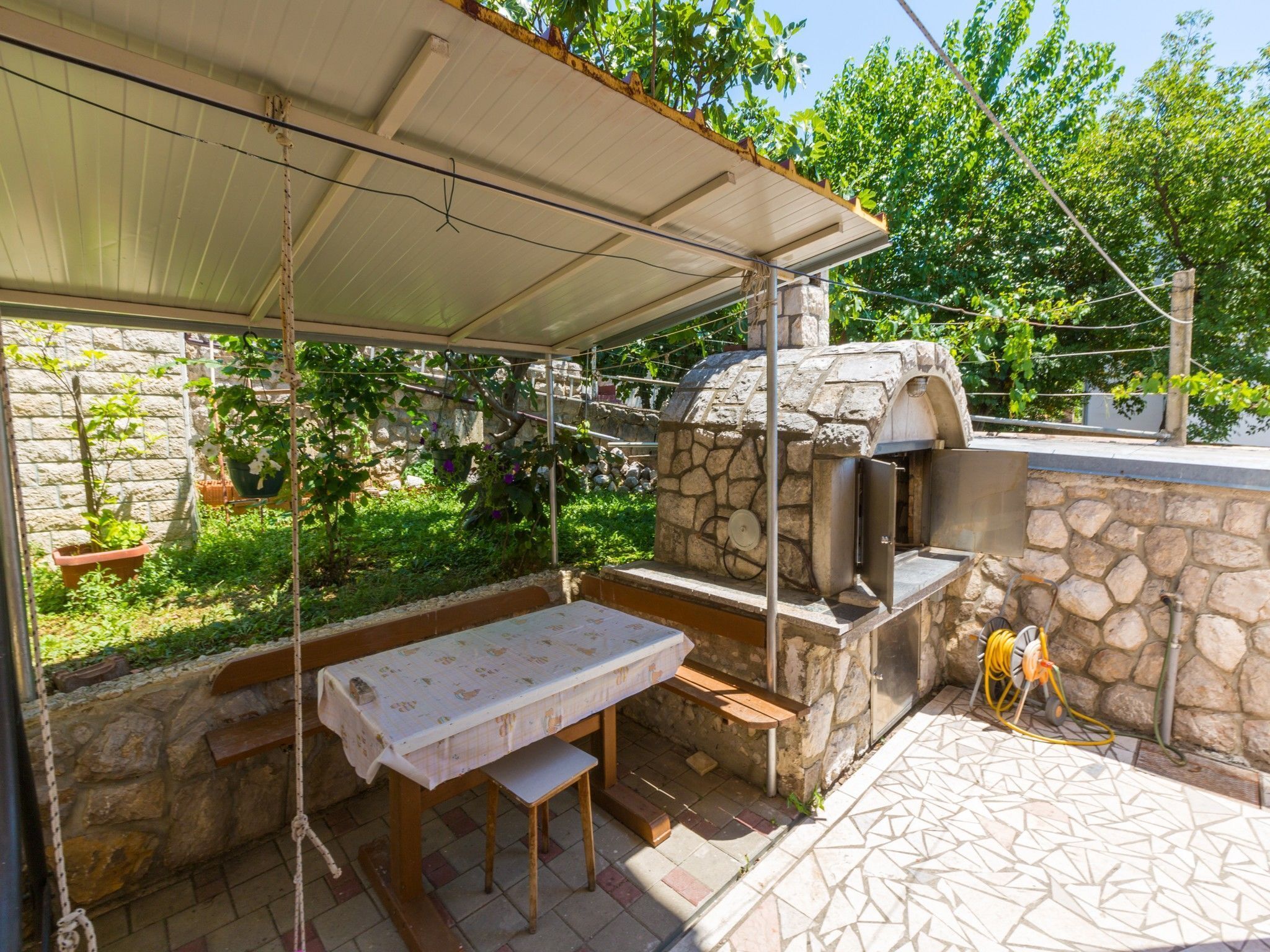 An outdoor patio with a stone barbecue grill, a covered table, and a bench.