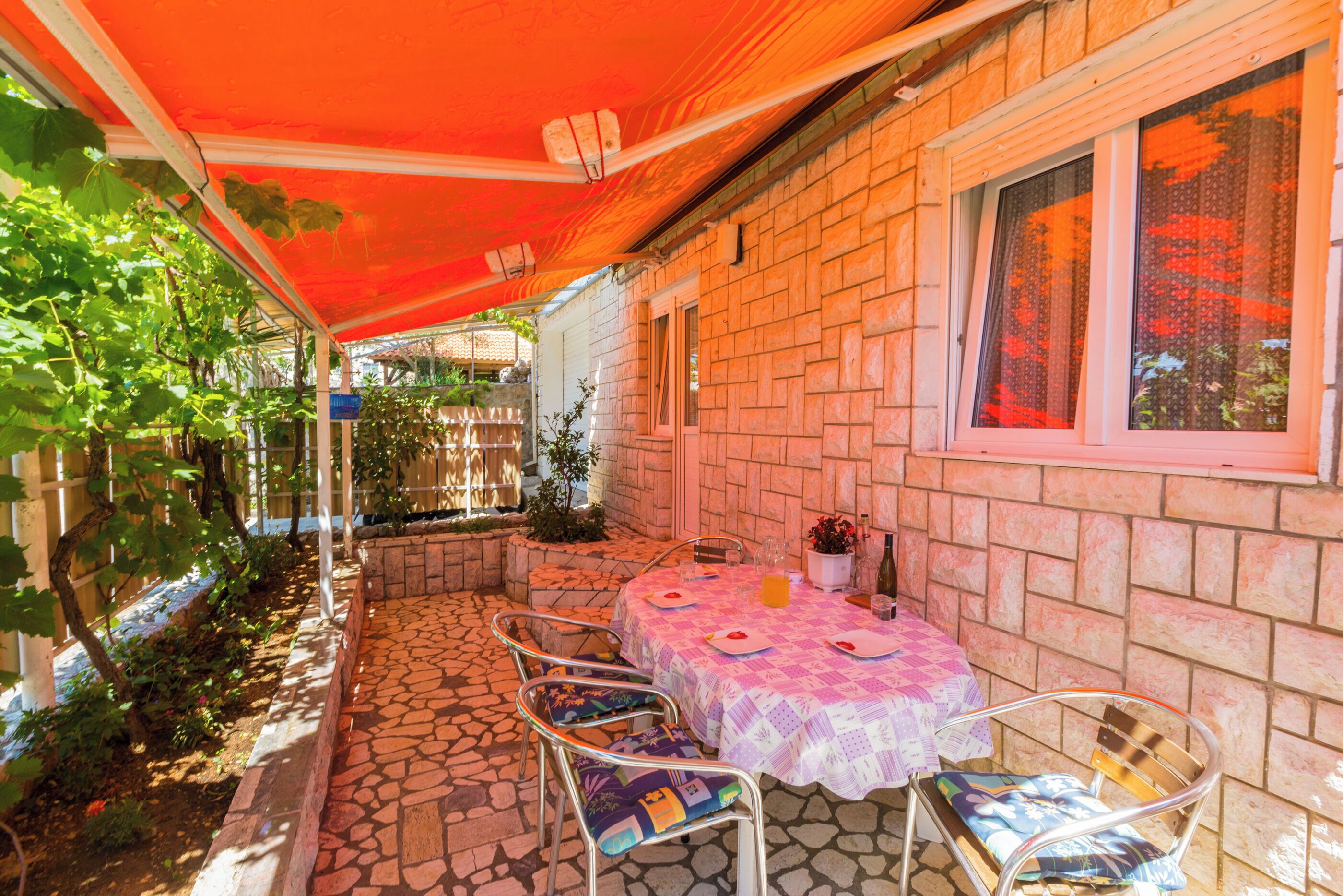 An outdoor patio with a table set for two, surrounded by stone flooring and metal chairs.
