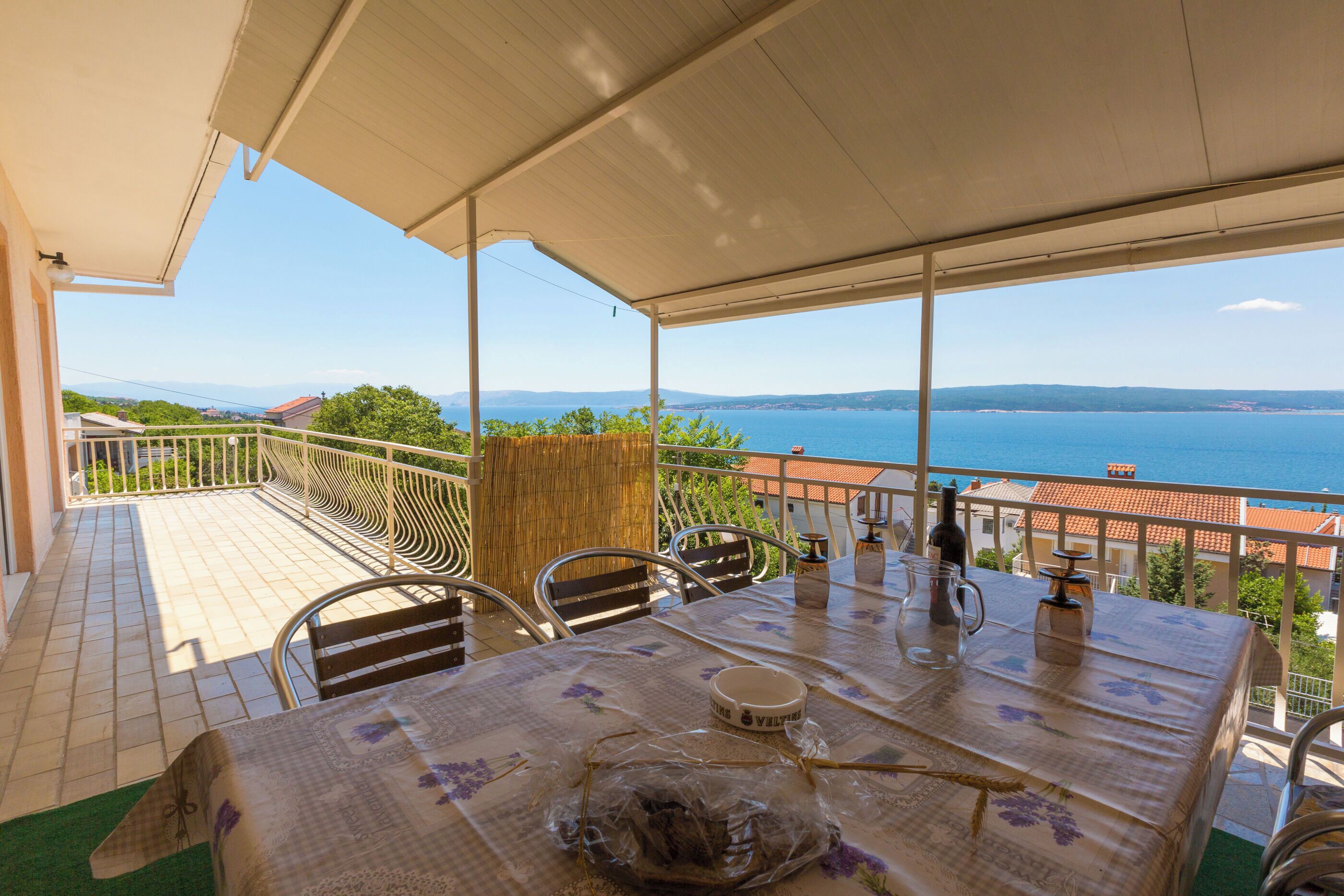 Una terraza techada con una mesa lista para comer, con vistas a un paisaje marino y montañas lejanas.