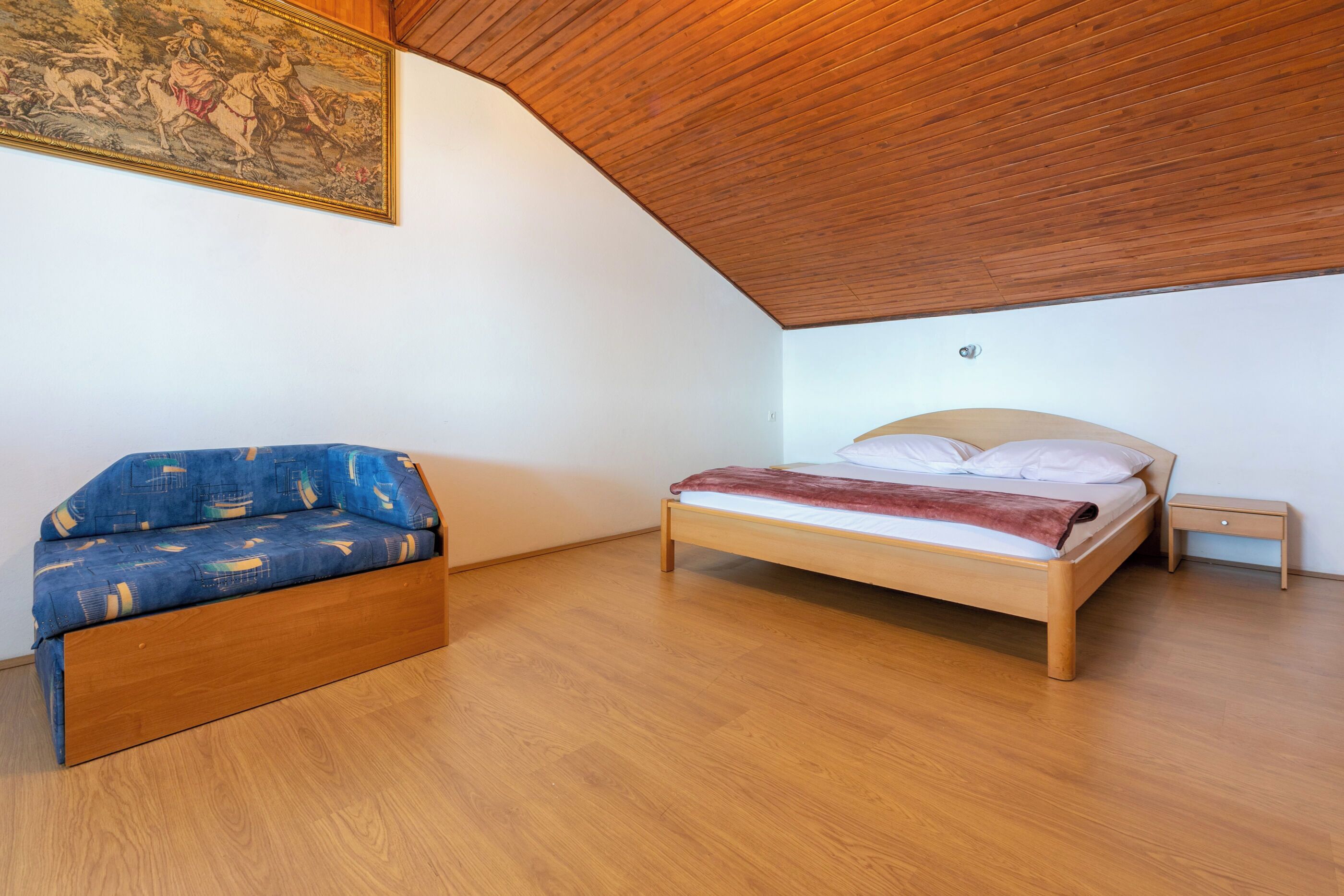 A bedroom with a bed, a sofa, a wooden ceiling, and a painting on the wall.