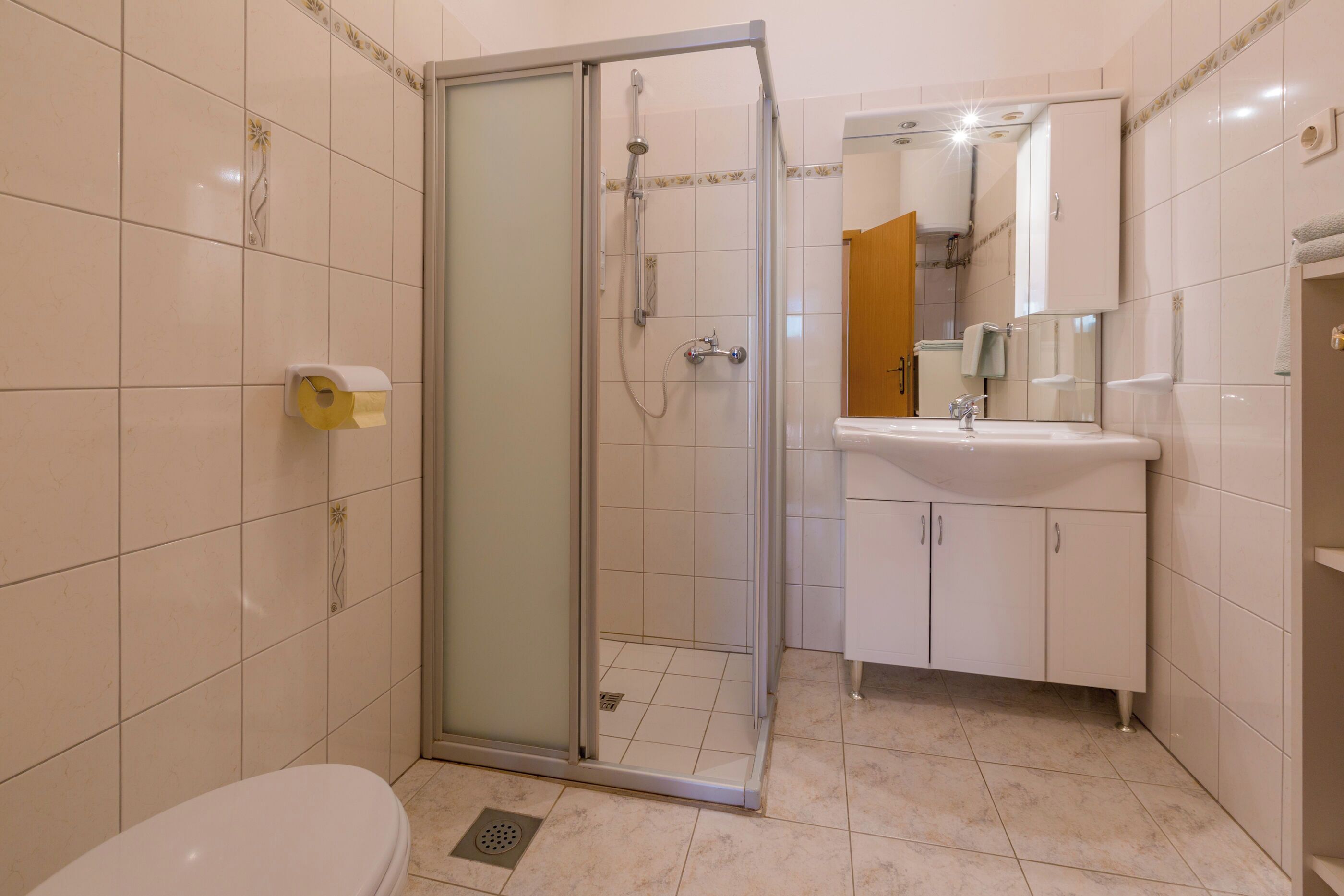 A bathroom with a glass-enclosed shower, a toilet, a sink, and a mirror.