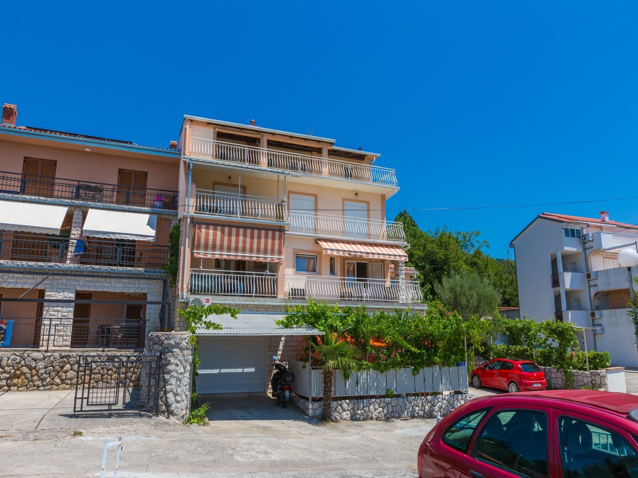 Um edifício residencial de vários andares com varandas, uma garagem e um carro vermelho estacionado na frente.