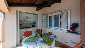 A dining area with a table set for two, a kitchen in the background, and a brick wall. - Apartments Matilda (Crikvenica)