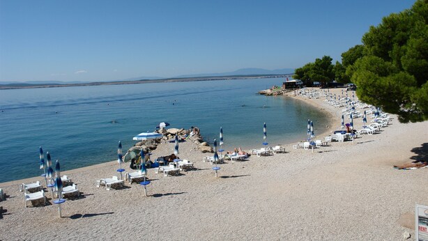 A beach with rows of sun loungers and umbrellas, a rocky shoreline, and a clear blue sky. - Apartments Matilda (Crikvenica)