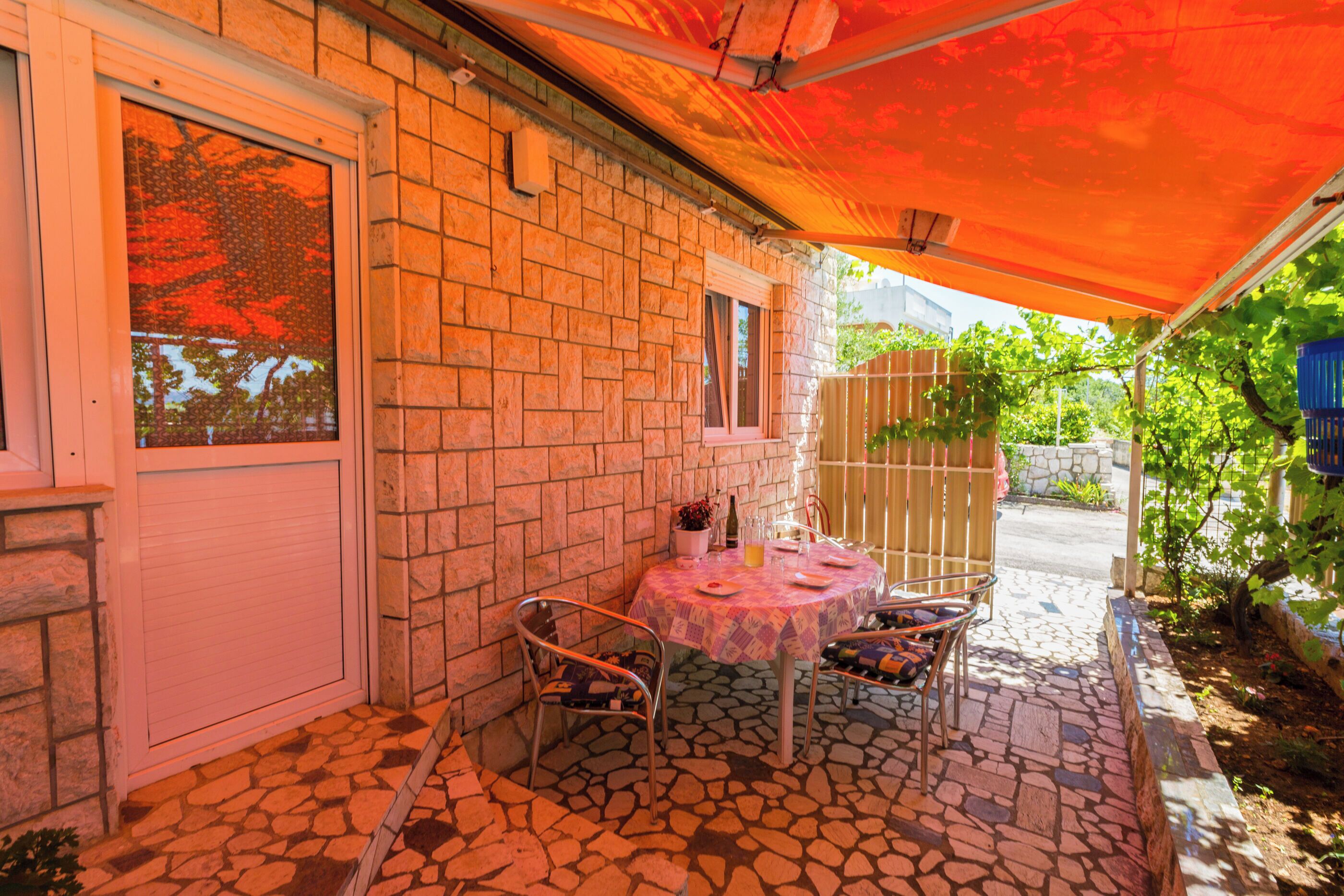 A patio with a stone floor, a round table, two chairs, and a covered area with an orange canopy.