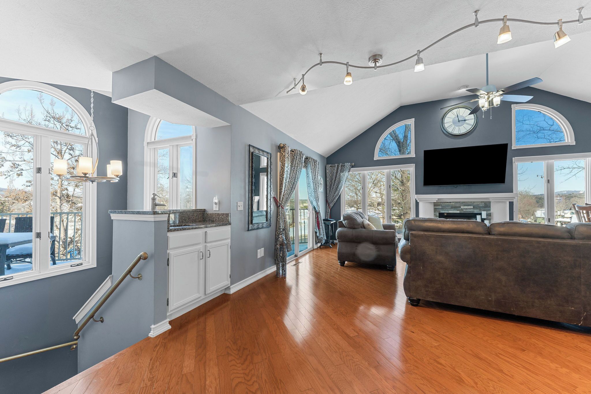 A spacious living room with hardwood floors, a large gray sofa, and a flat-screen TV.