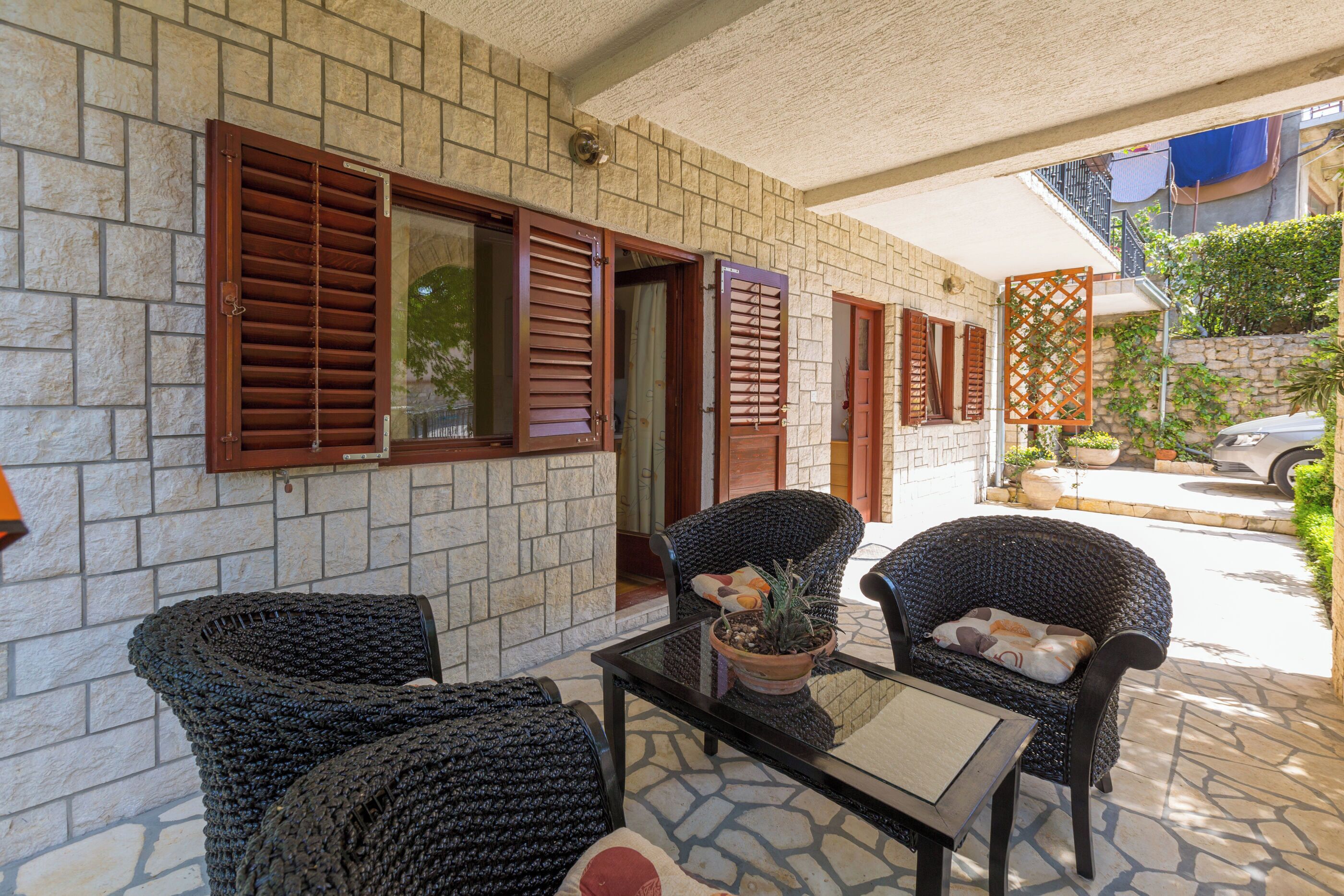 A patio with wicker furniture, a glass table, and a potted plant.