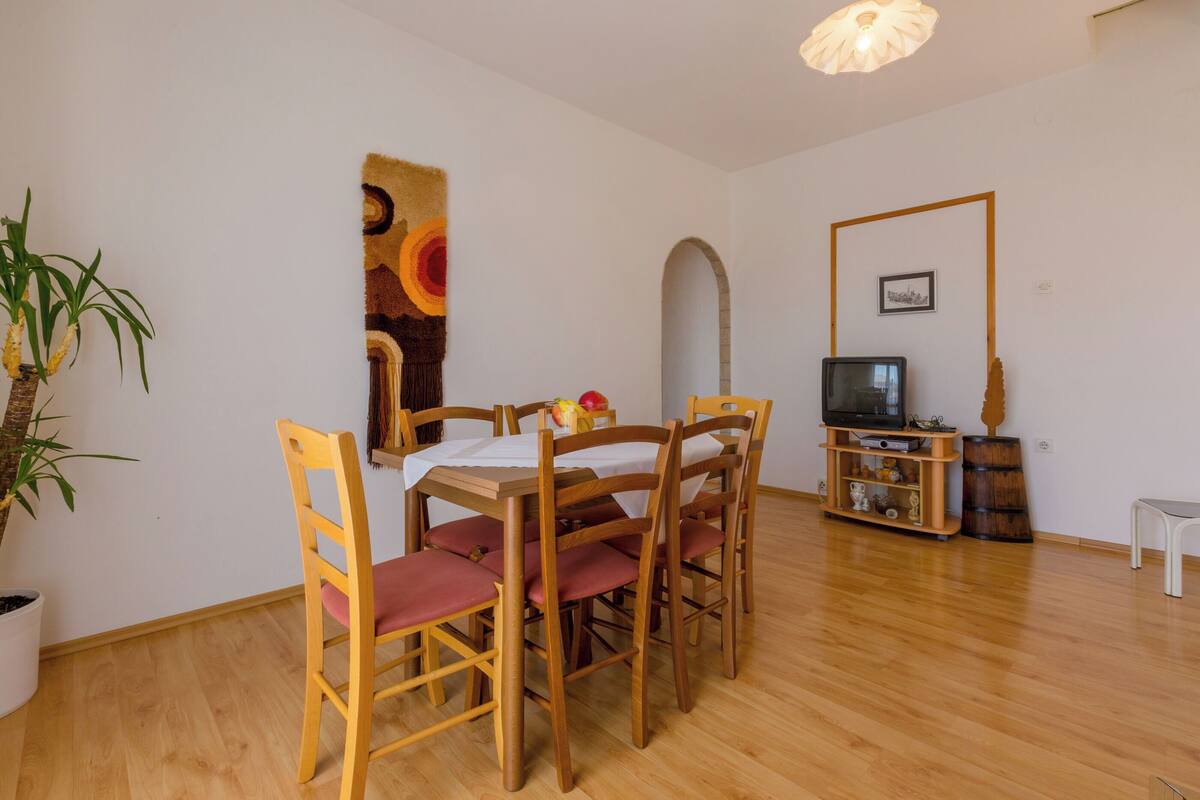 A dining area with a wooden table and chairs, a television, and a potted plant.