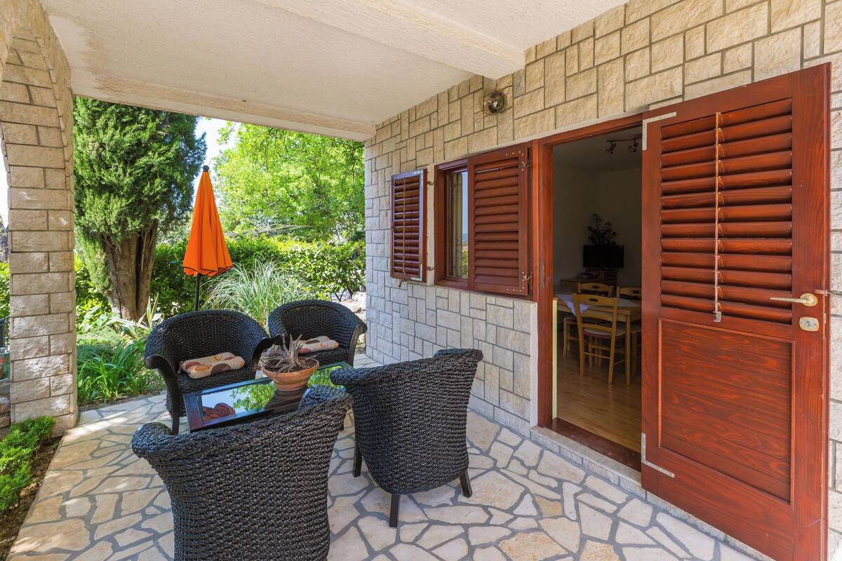 A covered patio with wicker furniture, a stone floor, and a wooden door.