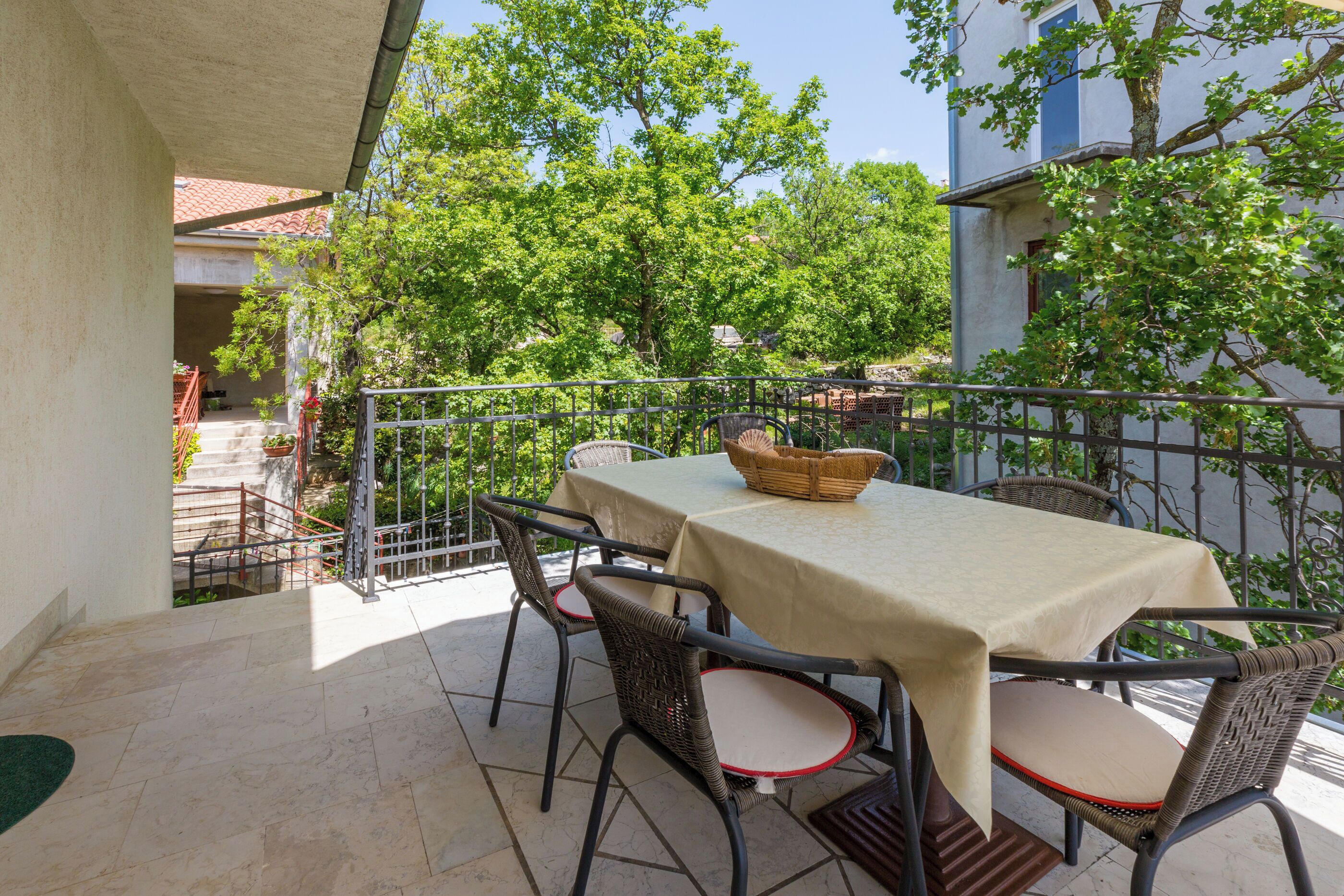 An outdoor patio with a table and chairs, surrounded by a metal railing and trees.