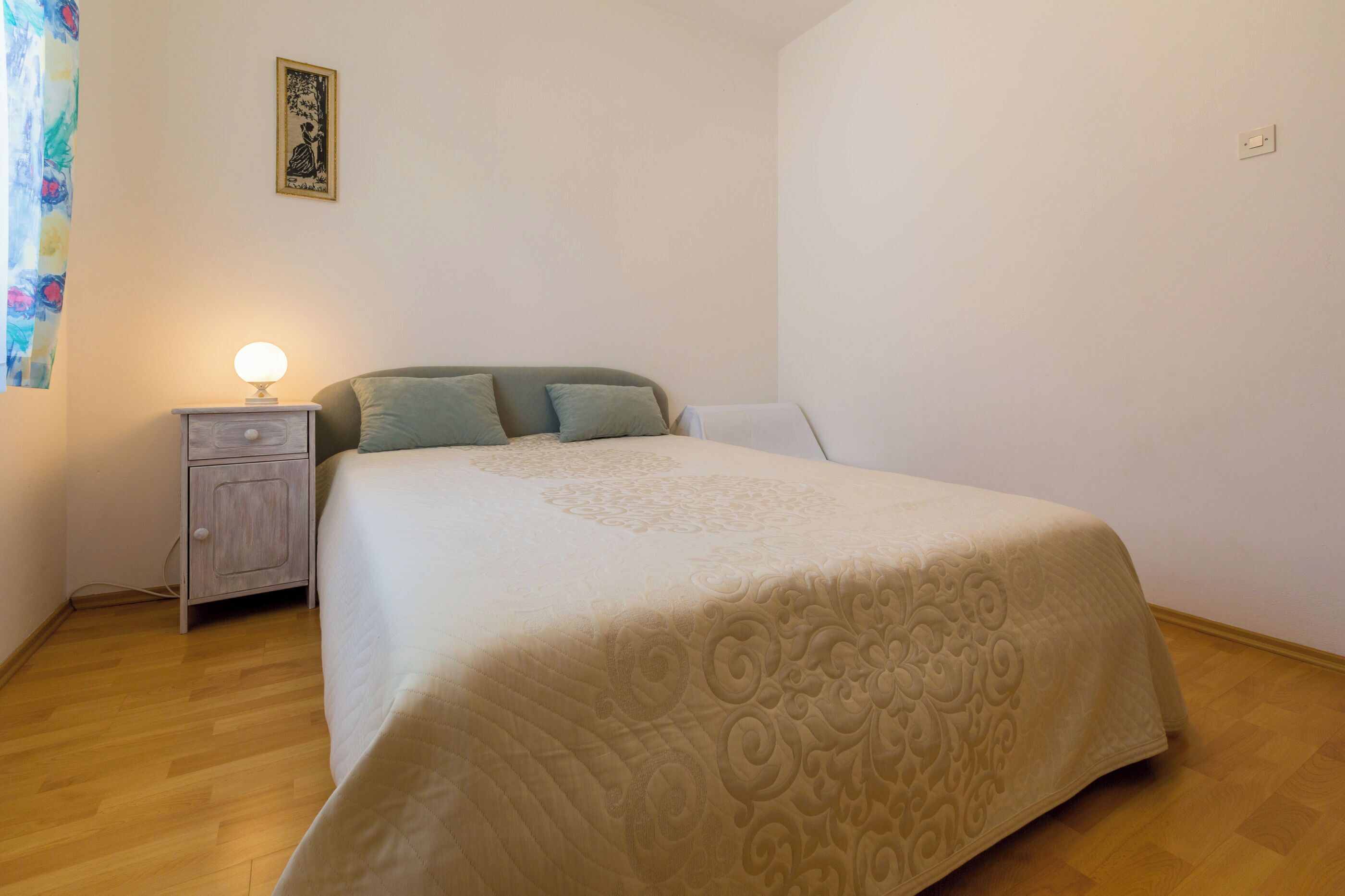 Une chambre à coucher avec un lit, une table de chevet, une lampe et un tableau accroché au mur.