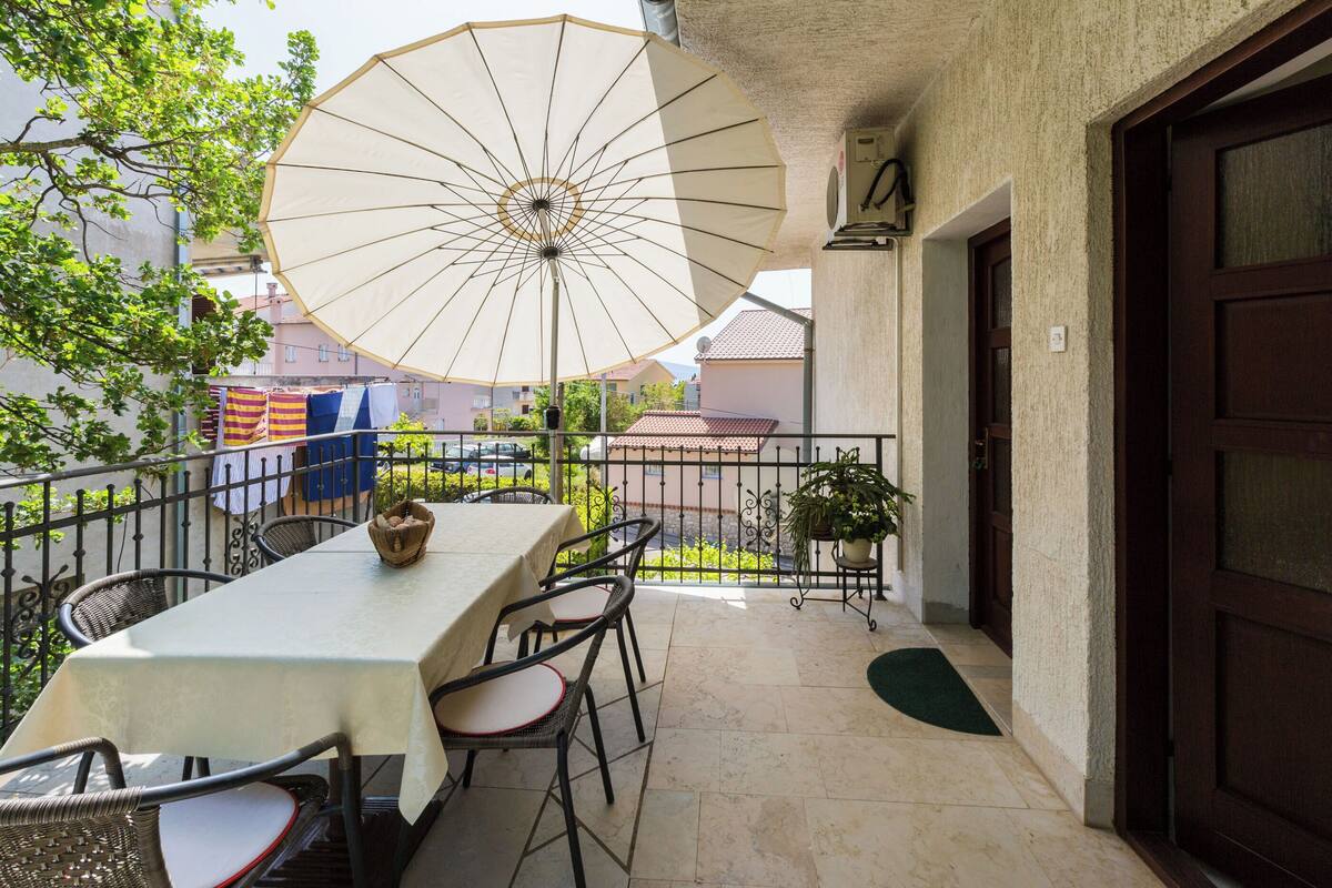 A balcony with a table and chairs, an umbrella, and a potted plant.
