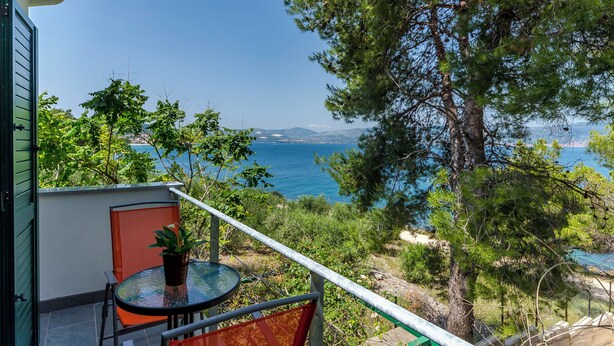 Un balcon avec une table et des chaises, donnant sur un paysage côtier avec des arbres et une vue sur la mer.
