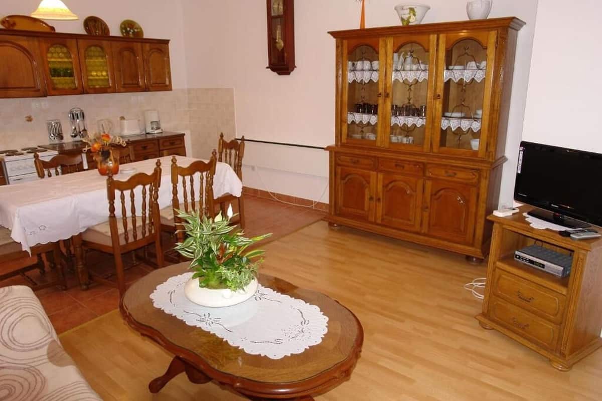 A living room with a dining table, chairs, a wooden cabinet, a television, and a plant on a table.