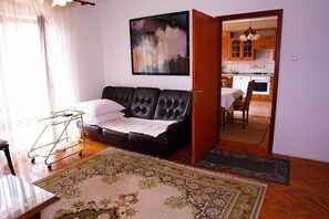 A living room with a black leather sofa, a small table, a rug, and a painting on the wall. - Apartments Nikolina (Novi Vinodolski)