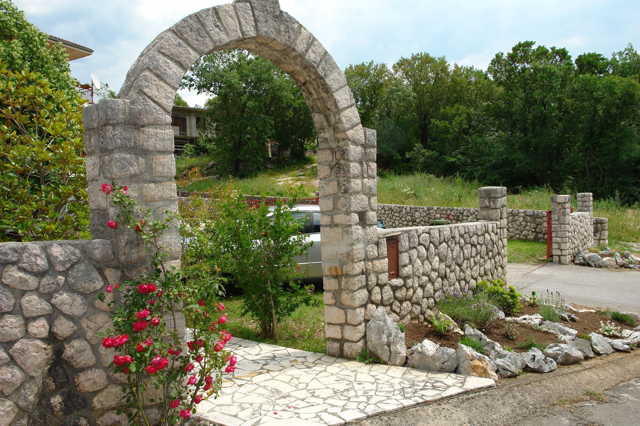 A stone archway leading to a house with a stone wall and a paved pathway.