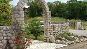 A stone archway leading to a house with a stone wall and a paved pathway. - Apartments Nikolina (Novi Vinodolski)